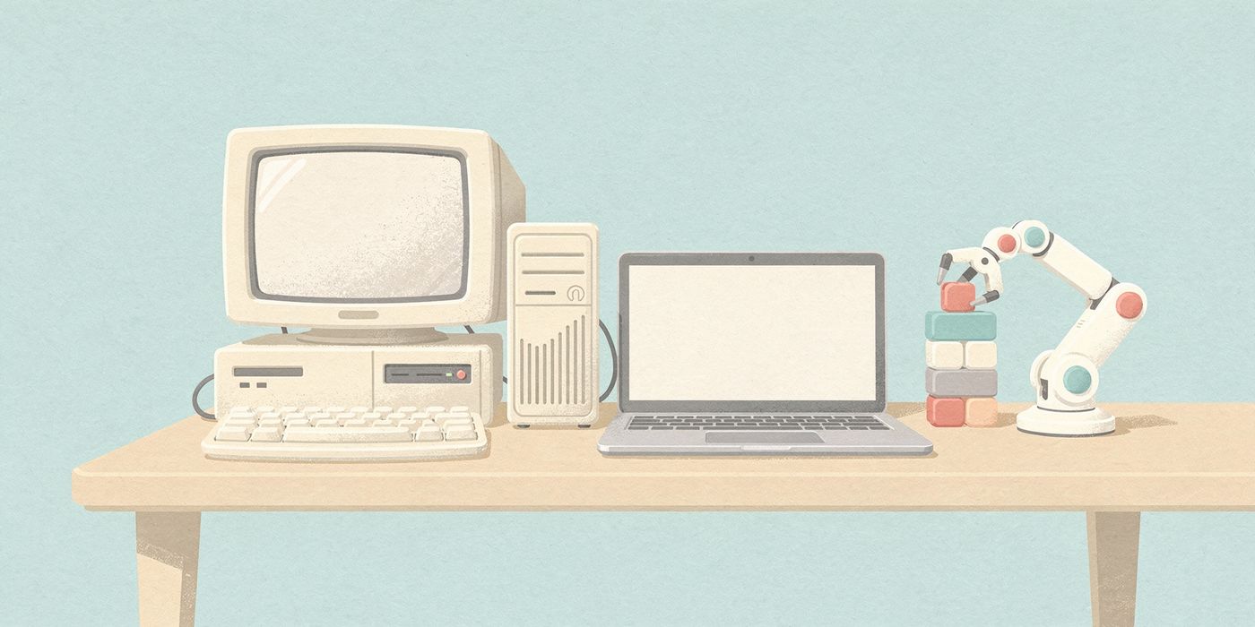 An old desktop computer beside a modern laptop and a small robot arm stacking blocks